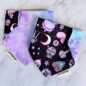 May include: Two purple and black dog bandanas with a galaxy print and a spooky, mystical print. The bandanas feature the text "I see through you" and "Goodbye" on them. The bandanas are made by the company "Paw's Payaya".