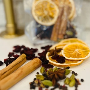May include: A close-up of a white surface with a variety of ingredients for making mulled wine. The ingredients include dried orange slices, cinnamon sticks, cranberries, star anise, and cardamom pods.