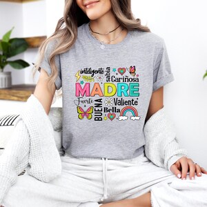 May include: A gray t-shirt with a colorful graphic design that says "MADRE" surrounded by words in Spanish, including "inteligente", "sabia", "cari&ntilde;osa", "fuerte", "buena", "valiente", and "bella".