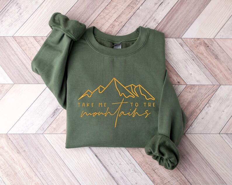 May include: A green sweatshirt with the text "Take me to the mountains" in yellow lettering and a stylised mountain range graphic.
