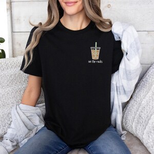 K&ouml;nnte beinhalten: Schwarzes T-Shirt mit einem Aufdruck eines braunen Eiskaffees mit Strohhalm und dem Text "on the rocks".