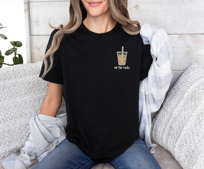 K&ouml;nnte beinhalten: Schwarzes T-Shirt mit einem Aufdruck eines braunen Eiskaffees mit Strohhalm und dem Text "on the rocks".