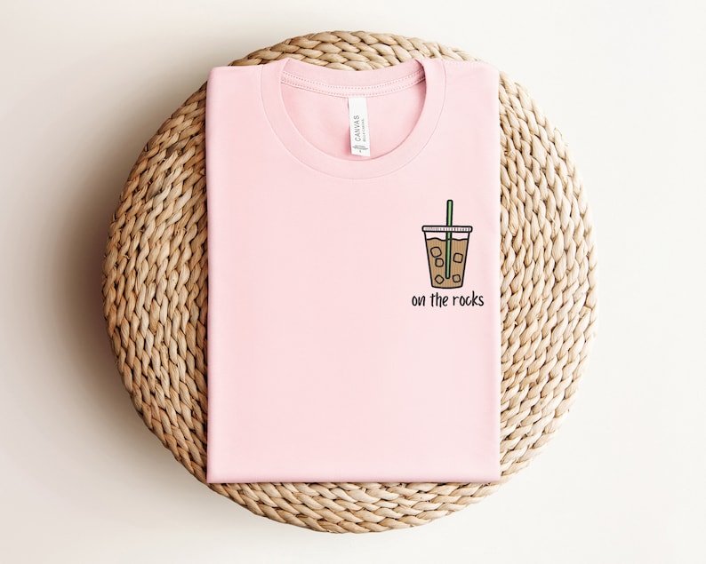 K&ouml;nnte beinhalten: Ein pinkfarbenes T-Shirt mit einer Grafik eines Glases mit Eiskaffee und dem Text "on the rocks".