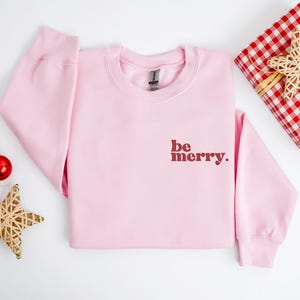 May include: Pink Christmas sweatshirt with the text "be merry." in red.