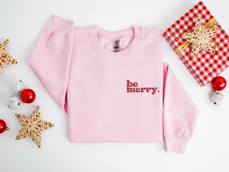 May include: Pink Christmas sweatshirt with the text "be merry." in red.
