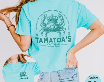Puede incluir: Una camiseta azul turquesa con un gráfico de un cangrejo con una corona. El texto "TAMATOA'S Crab Shack & Dinner Theater" está impreso debajo del cangrejo. El texto "FISH ARE DUMB, DUMB, DUMB THEY CHASE ANYTHING THAT GLITTERS" está impreso en un círculo alrededor del cangrejo. La camiseta está puesta en una modelo que lleva pantalones vaqueros azules. El color de la camiseta es "Chalky Mint."