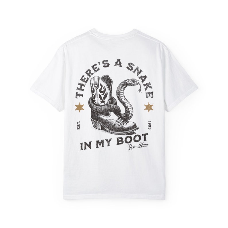 May include: White t-shirt with a black and white graphic print of a snake in a cowboy boot. The graphic includes the text "There's a Snake in My Boot" and "Yee-Haw".