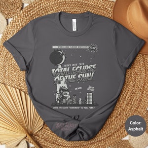 May include: A dark gray t-shirt with a vintage comic book style graphic featuring a total eclipse of the sun. The graphic includes a dinosaur-like creature and the text "There was this Total Eclipse of the Sun!"  "Da Doo!" and "Shoop Da Doo!"  The text "Does this look "Inanimate" to you, punk?" is at the bottom of the graphic.