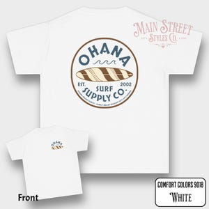 May include: White t-shirt with a circular graphic on the back that reads "OHANA SURF SUPPLY CO." with a surfboard illustration. The front of the shirt has a smaller version of the same design. The text "COMFORT COLORS 9018 White" is in the bottom right corner.