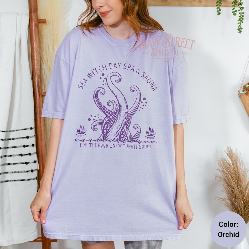 May include: Purple t-shirt featuring a graphic of an octopus with the text "Sea Witch Day Spa & Sauna Est. 1989 For the Poor Unfortunate Souls".