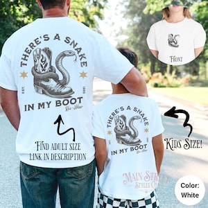 May include: White t-shirt with a graphic of a snake in a cowboy boot and the text "There's a Snake in My Boot Yee-Haw". The shirt is available in adult and kids sizes.