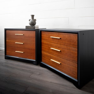 May include: Two black and brown wooden dressers with gold drawer pulls. The dressers have three drawers each. The dressers are sitting on a dark wood floor.