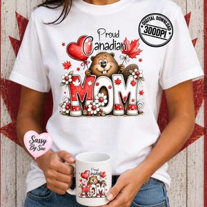 Könnte beinhalten: Weißes T-Shirt mit einer Grafik, die einen Biber mit einem Ahornblatt und einem herzförmigen Ballon zeigt. Der Text lautet "Proud Canadian MOM" in Rot und Weiß. Eine passende Tasse wird in den Händen gehalten.