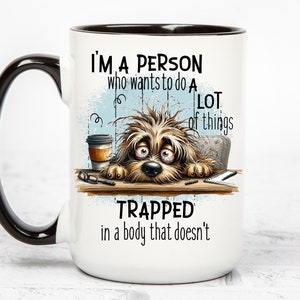 Pu&ograve; includere: Tazza da caff&egrave; in ceramica bianca con manico e bordo neri. La tazza presenta un'illustrazione di un cane con una tazza di caff&egrave; e il testo "Sono una persona che vuole fare molte cose intrappolata in un corpo che non lo fa".