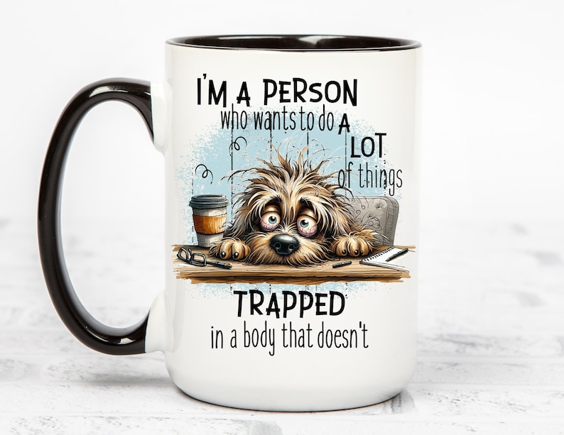Pu&ograve; includere: Tazza da caff&egrave; in ceramica bianca con manico e bordo neri. La tazza presenta un'illustrazione di un cane con una tazza di caff&egrave; e il testo "Sono una persona che vuole fare molte cose intrappolata in un corpo che non lo fa".