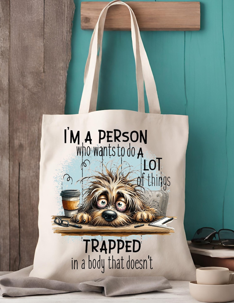 Pu&ograve; includere: Una borsa di tela bianca con un'illustrazione di un cane di cartone animato e il testo "Sono una persona che vuole fare molte cose intrappolata in un corpo che non lo fa".