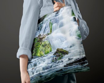 May include: A tote bag with a colorful image of a waterfall cascading over moss-covered rocks. The bag is made of a durable canvas material and features a long, adjustable strap.