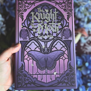 Può includere: Un libro con copertina rigida intitolato The Knight & The Moth di Rachel Gillig con una copertina viola raffigurante una grande falena, illustrazioni di archi gotici e figure di gargoyle. Il design include intricate linee nere.