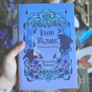May include: A purple book with a blue and white design. The title is "Iron Flame" and the subtitle is "The Empyrean Series". The author is "Rebecca Yarros".