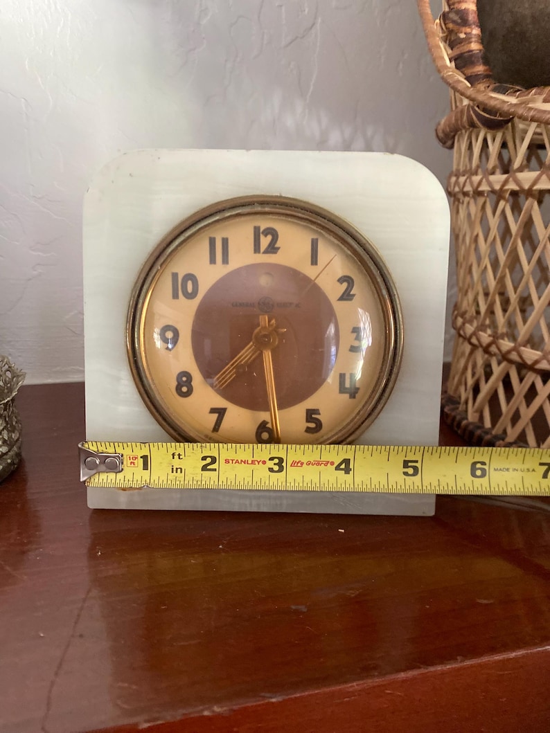 May include: A vintage white marble clock with gold accents and a round face. The clock face has black Roman numeral hour markers and black hands. The clock is 1 inch tall.
