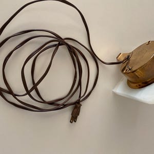 May include: A white marble base with a brass clock face and a brown electrical cord.