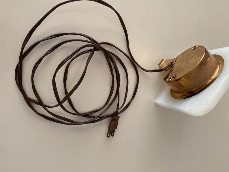 May include: A white marble base with a brass clock face and a brown electrical cord.