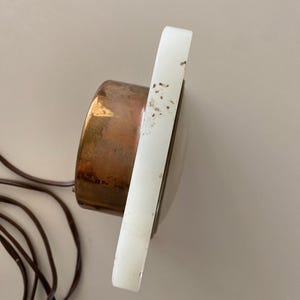 May include: A white alabaster clock with a copper face and a cord. The clock is on a white background.