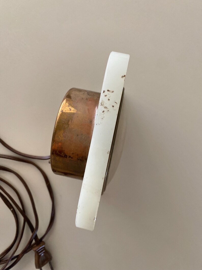 May include: A white alabaster clock with a copper face and a cord. The clock is on a white background.