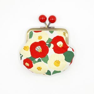 May include: A small, white and red floral patterned coin purse with a gold metal frame and red plastic clasps.