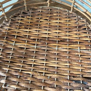 May include: A woven wicker basket with a round, flat bottom. The basket is made of natural brown wicker and has a light brown woven pattern.
