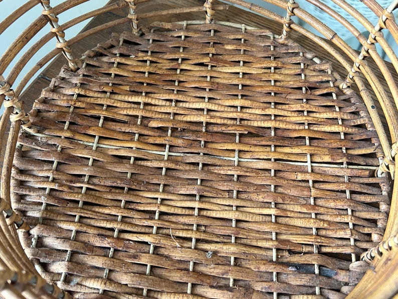 May include: A woven wicker basket with a round, flat bottom. The basket is made of natural brown wicker and has a light brown woven pattern.