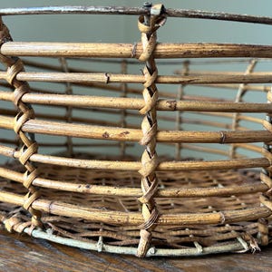 May include: A woven wicker basket with a white painted rim. The basket is made of natural brown bamboo and has a round shape.