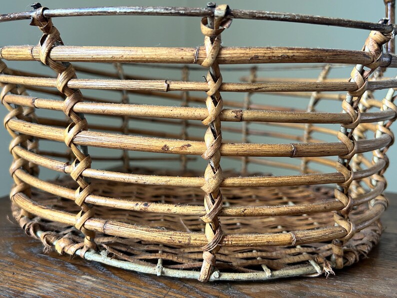 May include: A woven wicker basket with a white painted rim. The basket is made of natural brown bamboo and has a round shape.