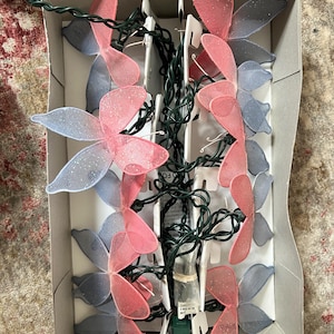 May include: A string of fairy lights with pink and blue butterfly-shaped covers. The lights are in a white box with a green wire.
