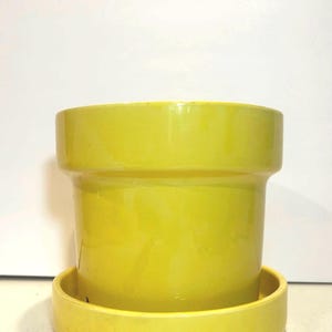 May include: A yellow ceramic planter with a matching saucer. The planter has a simple, rounded design.