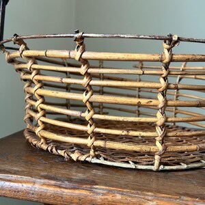 May include: A woven wicker basket with a metal frame and handle. The basket is oval shaped and has a natural brown color.