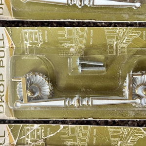 May include: Vintage cabinet drop pulls with white and gold detailing. The pulls feature a decorative, fan-shaped design and are packaged with screws. The packaging includes the text "Only Cabinet Accessories DROP PULL".