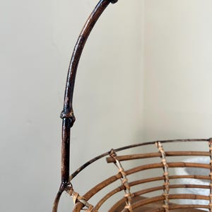 May include: A brown wicker basket with a dark brown wooden handle. The basket is woven with a circular pattern and has a wide, open top.