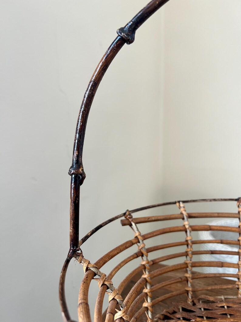 May include: A brown wicker basket with a dark brown wooden handle. The basket is woven with a circular pattern and has a wide, open top.