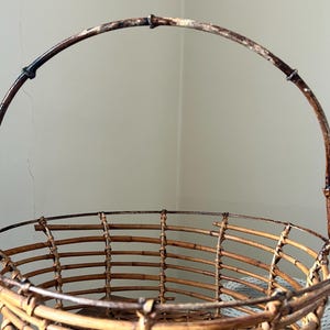 May include: A brown wicker basket with a wire handle. The basket is made of woven bamboo and has a round shape.