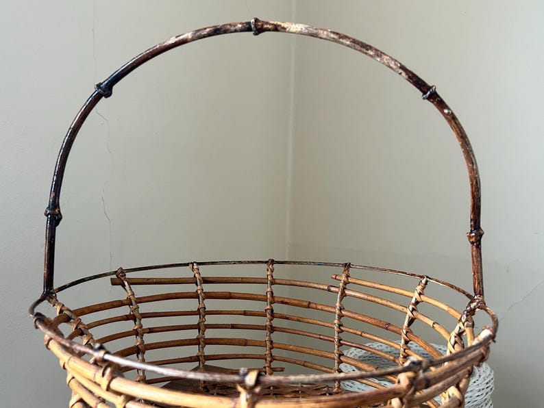 May include: A brown wicker basket with a wire handle. The basket is made of woven bamboo and has a round shape.