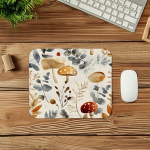 May include: A rectangular mousepad featuring a watercolor design of mushrooms, leaves, and berries in shades of brown, orange, red, and gray on a cream background. The mousepad is on a wooden desk next to a white mouse and keyboard.