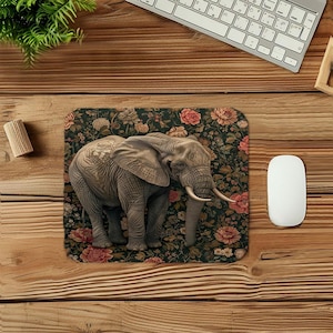 May include: A rectangular mousepad featuring a detailed illustration of an elephant with tusks. The elephant is set against a dark background with a floral pattern of pink and cream-colored flowers. A white computer mouse and keyboard are visible.