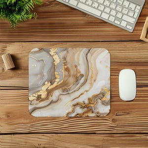 May include: Square mousepad with a marble design in shades of white, gray, and gold. The pattern features flowing lines and gold leaf accents. A white computer mouse is next to the mousepad on a wooden desk.