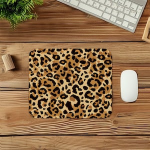 May include: A rectangular mousepad with a leopard print design in shades of brown and black. A white computer mouse is to the right of the mousepad. A keyboard and other office supplies are in the background.