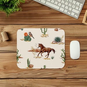 May include: A rectangular mousepad with a desert-themed design. The beige surface features illustrations of cacti, a brown horse, a bird, and other desert plants. The mousepad is surrounded by a wooden desk, a keyboard, and a computer mouse.
