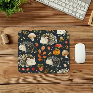 Peut inclure: Un tapis de souris rectangulaire avec un motif fantaisiste de hérissons, de champignons, de fraises et de feuilles d'automne sur un fond bleu foncé. Le motif comprend une citrouille et divers éléments botaniques, créant un thème saisonnier.