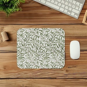 May include: A rectangular mousepad featuring a repeating pattern of green leaves and vines on a white background. The design is reminiscent of a botanical illustration. The mousepad is on a wooden surface, with a computer mouse and keyboard visible.