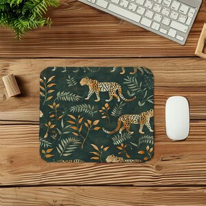 May include: A rectangular mousepad with a dark green background featuring a repeating pattern of leopards and foliage in shades of orange, tan, and green. The mousepad is surrounded by a wooden desk, a keyboard, and a computer mouse.