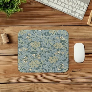Peut inclure: Tapis de souris rectangulaire avec un motif floral dans les tons de bleu, vert et crème. Le motif présente des fleurs et des feuilles stylisées. Une souris d'ordinateur et un clavier blancs sont visibles en arrière-plan.